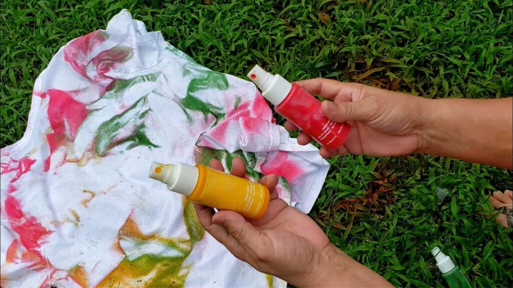 Step 2: a pair of hands holding small tie dye party spray bottles over a shirt