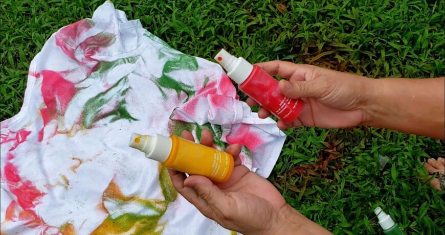 Step 2: a pair of hands holding small tie dye party spray bottles over a shirt