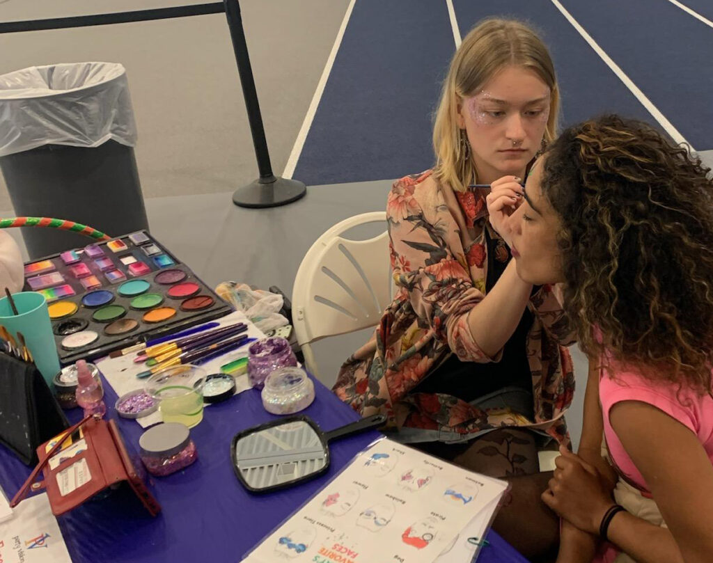 Derry NH face painter, balloon twister, bubble performer, and children's party entertainer Thea face painting a client at an event inside a gym